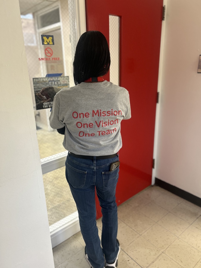 Staff member showing off the back of their staff apprieciation shirt that reads, One Mission, One Vision One Team