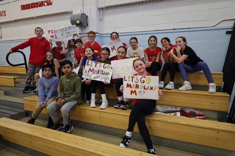 Students holding signs on gymnasium bleachers.