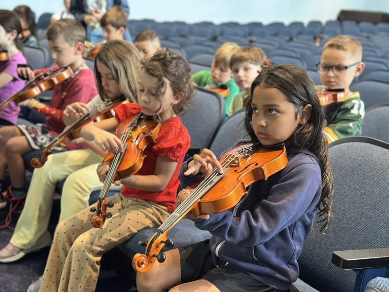 many students in auditorium playing violins