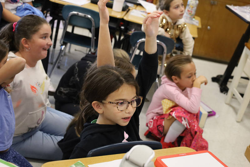 students in classroom raise hands