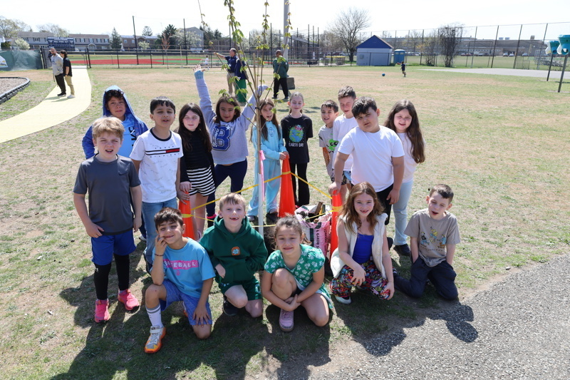 Children participating in a tree planting event, gathered around a young tree as they learn about nature and teamwork.