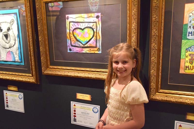 Student standing proudly in front of art exhibit.