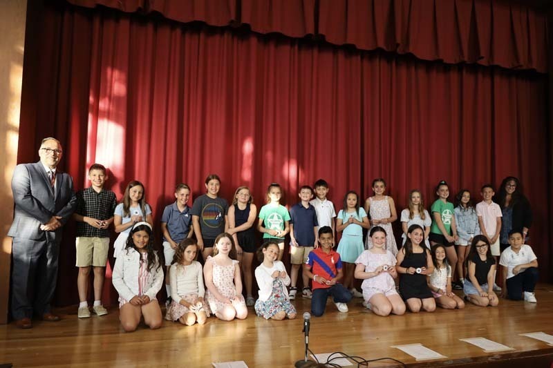 Students on stage in front of red curtain.