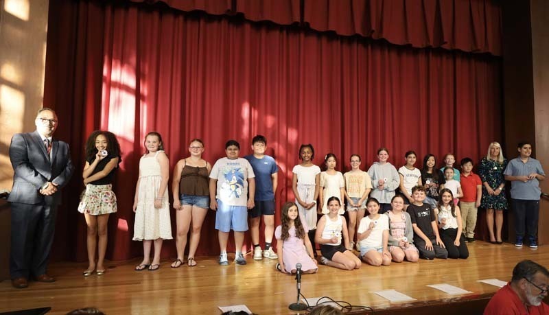 Students on stage in front of red curtain.