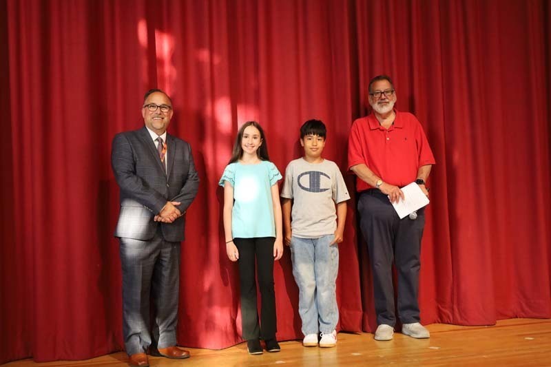 Students on stage in front of red curtain.