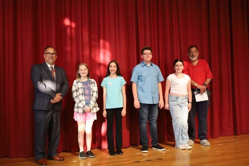 Students on stage in front of red curtain.