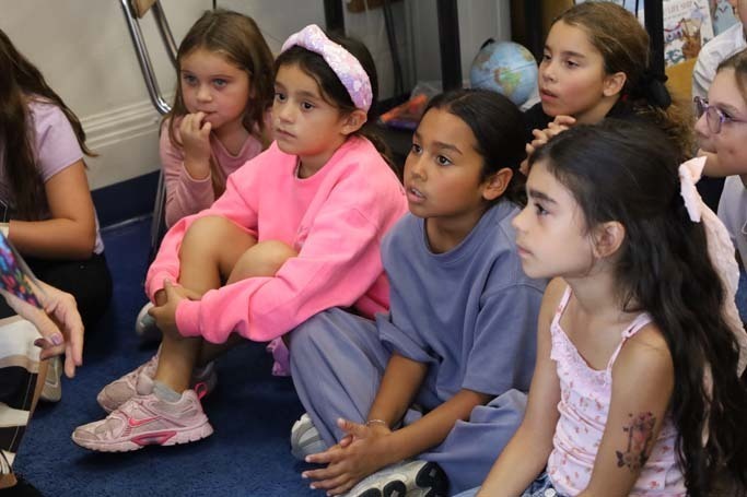 Students sitting on the ground listening to teacher.
