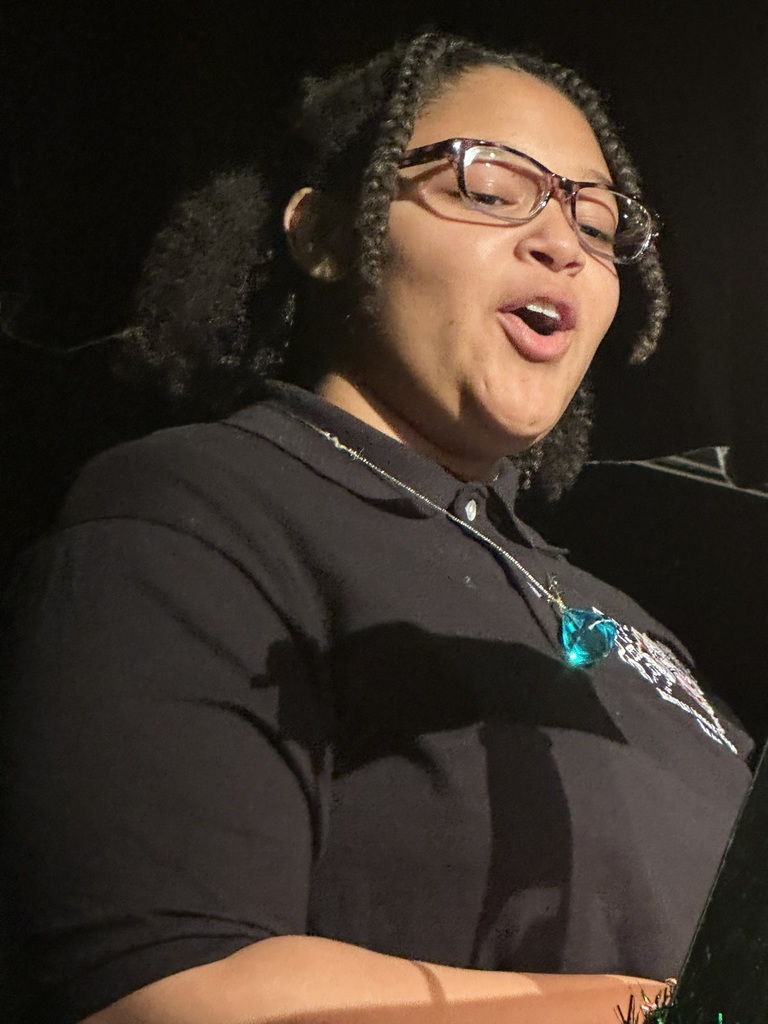 The image shows a student speaking at the band concert.