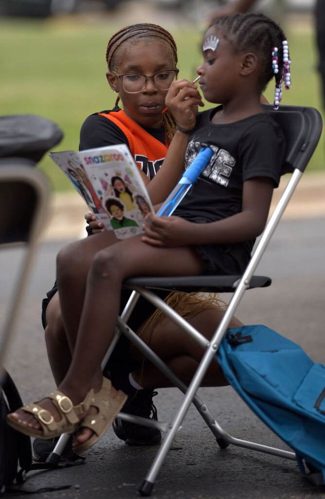 A young student getting her face painted while seated at a BHAS community event.