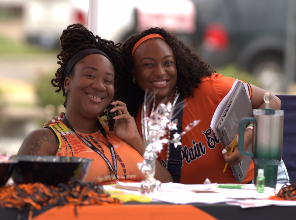Two smiling Benton Harbor Area Schools staff members posing together behind an information table at an outdoor event.