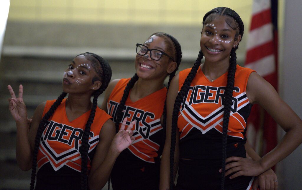 Three Benton Harbor cheerleaders in orange and black uniforms smiling and posing together at a school event.