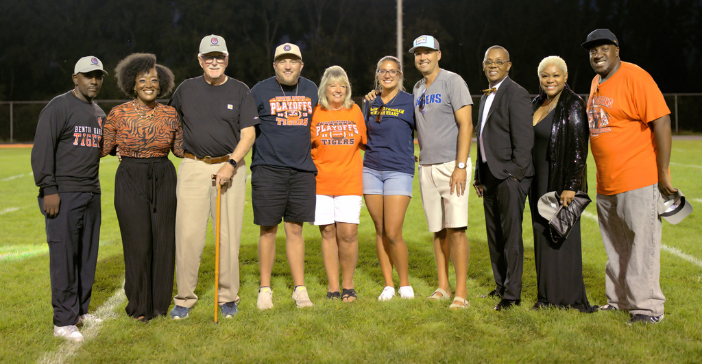 Former Benton Harbor football coaches & families, staff, and supporters posing together on the field during a playoff team celebration.