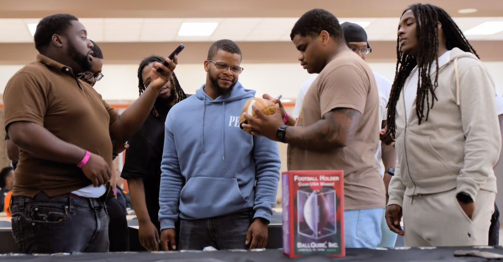 Former Benton Harbor football players gathering around a table as a commemorative football is signed during the reunion.