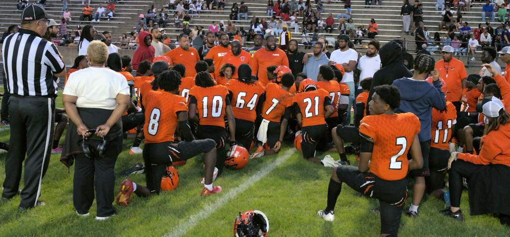 Benton Harbor Tigers football players, coaches, and former players gathered in a large team huddle on the field.