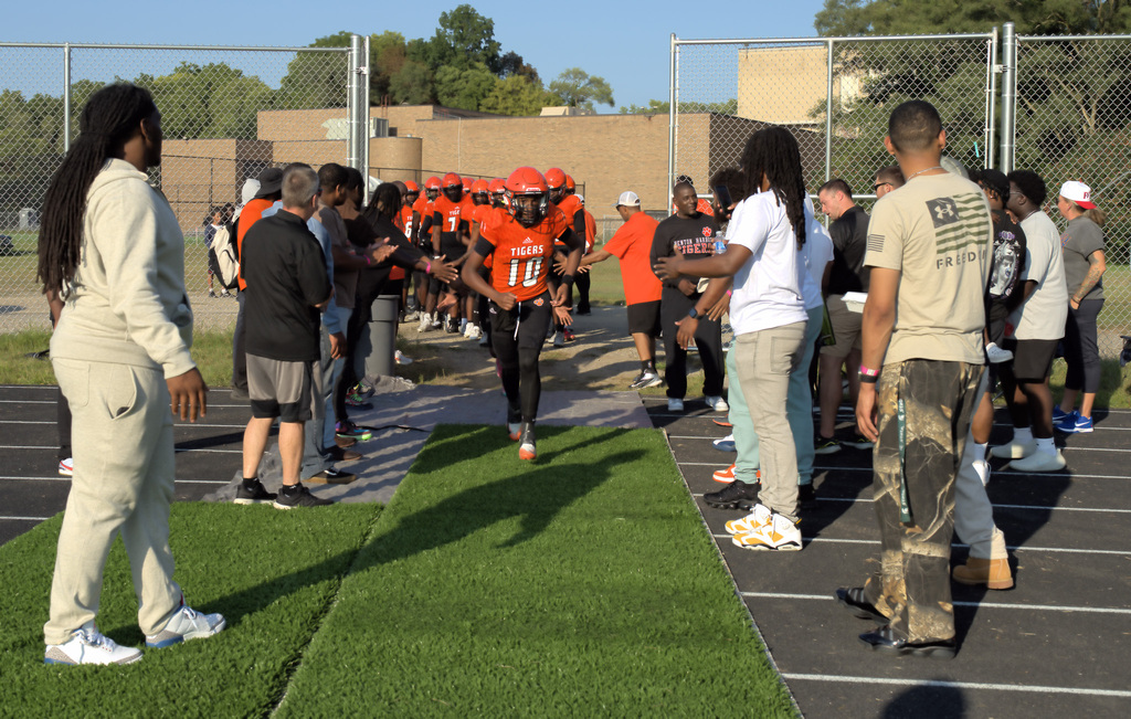 Benton Harbor Tigers football players entering the field as former players and supporters welcome them from both sides.