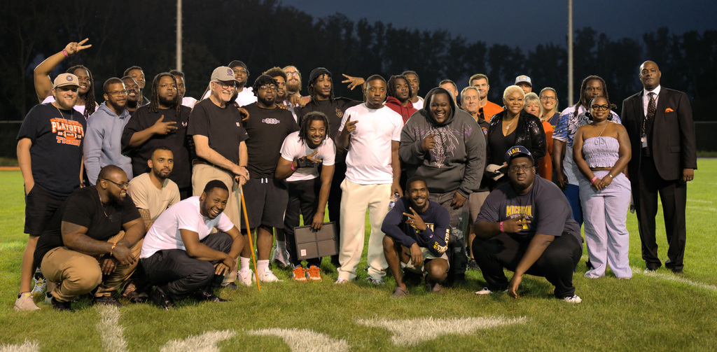 Former Benton Harbor football players, coaches, staff, and supporters posing together on the field during a playoff team reunion.