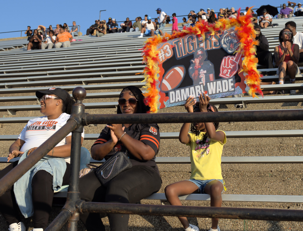 Benton Harbor Tigers fans cheering from the bleachers while holding a decorated sign supporting a football player.