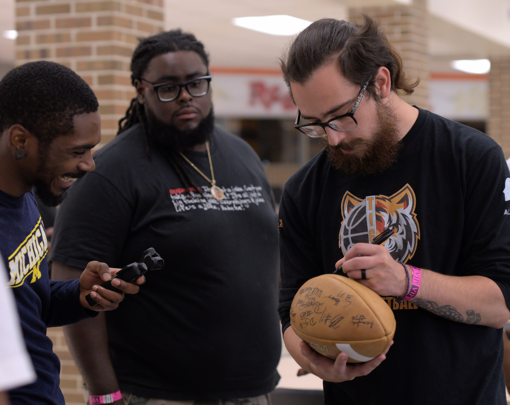 Former Benton Harbor football players gathering as one signs a commemorative football during the playoff team reunion.
