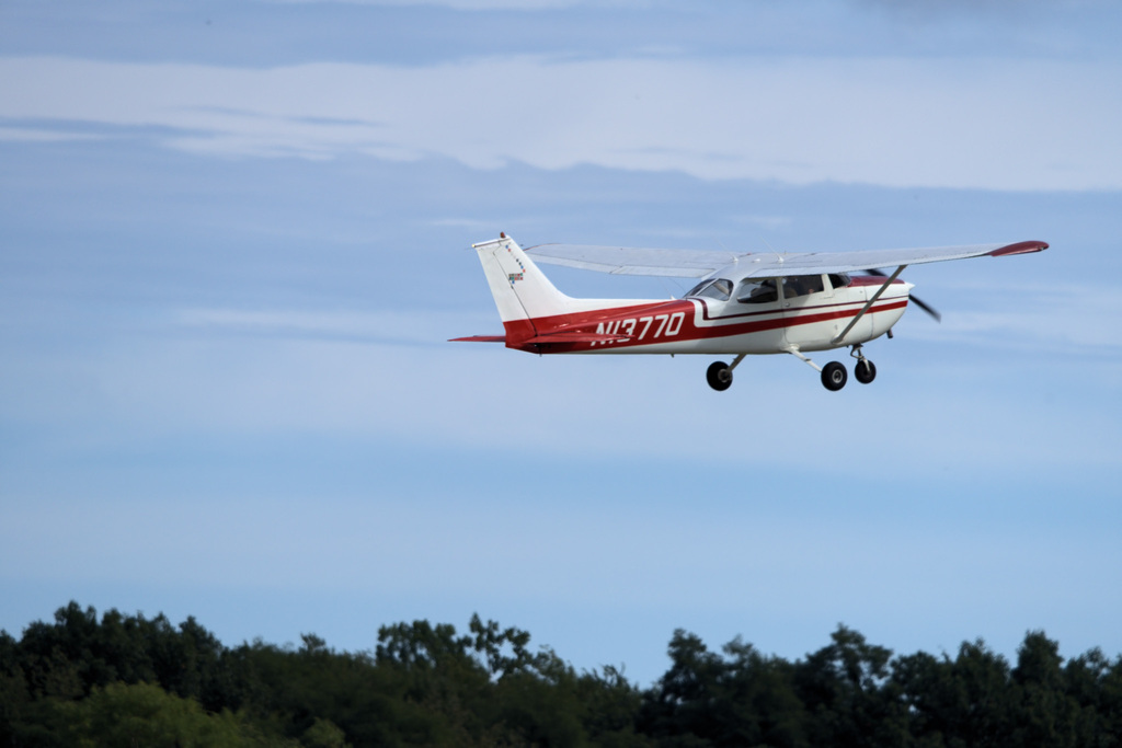 Red-and-white training aircraft flying above the airport during a student aviation experience.