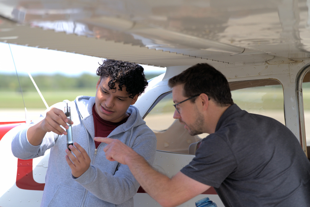Student examining an aircraft component with guidance from an aviation instructor.