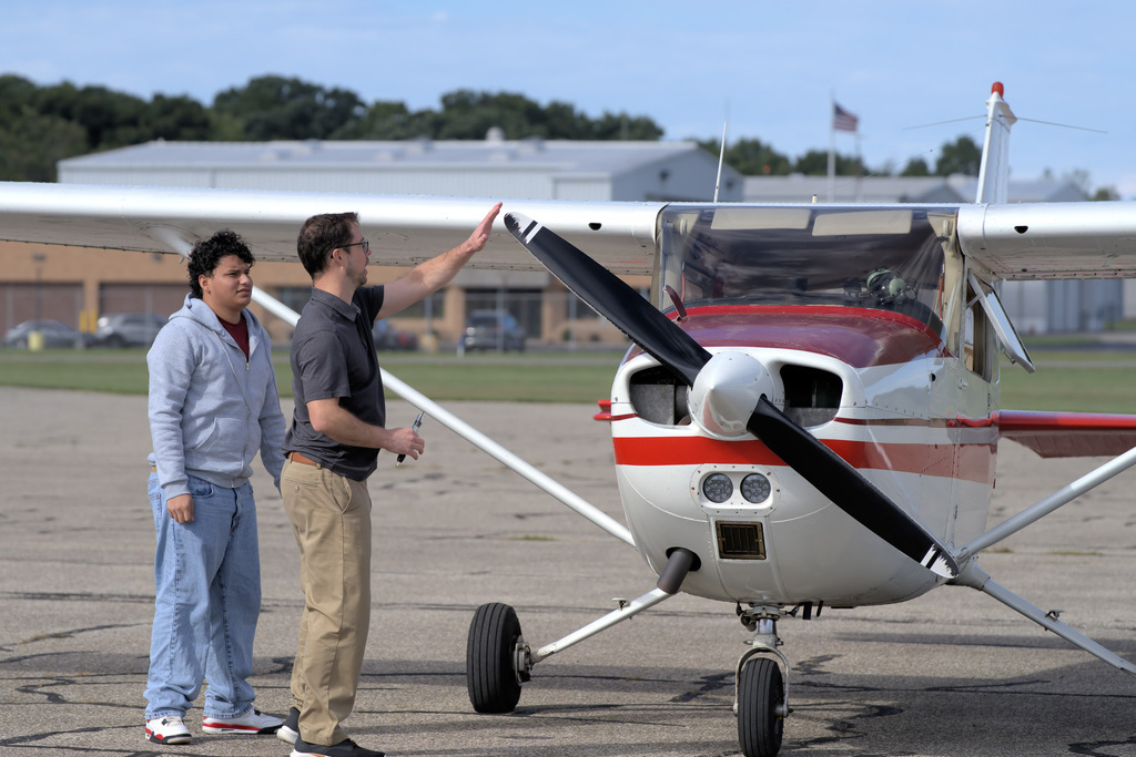 Student and aviation instructor inspecting the propeller area of a training aircraft before flight.
