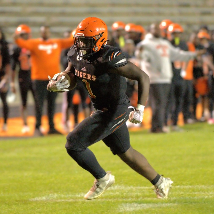 Benton Harbor Tigers football player wearing number 1 runs with the football during a nighttime game.