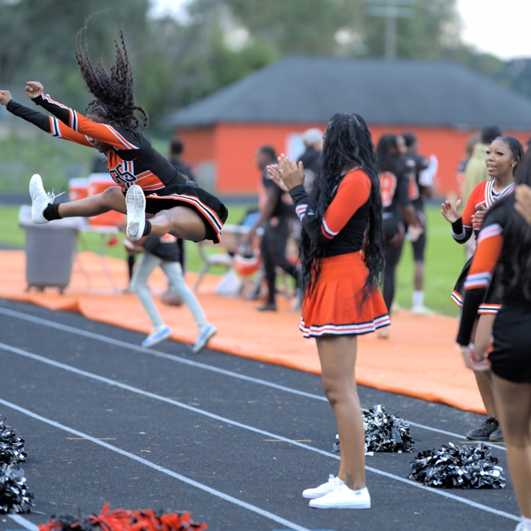 Benton Harbor Tigers cheerleader performs a toe-touch jump while teammates cheer and clap along the sideline.