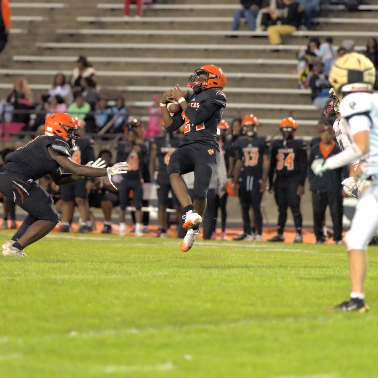 Benton Harbor Tigers football player leaps into the air to catch a pass as opposing players in white and green uniforms approach.