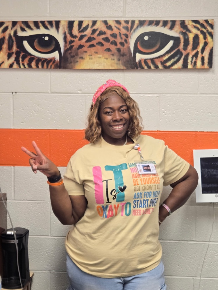 principal Patterson standing in front of a tiger eye banner, with a peace sign pose