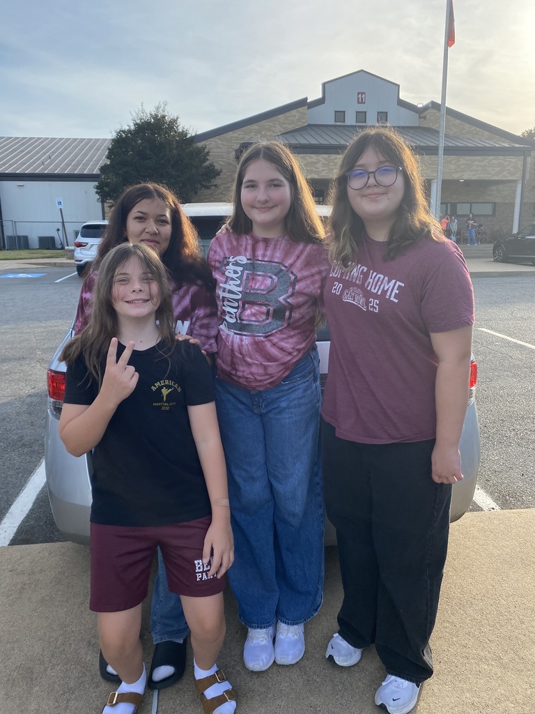 A group of four students are posing in front of Benton Middle School as they wait for the senior parade to start. One student is holding up a peace sign with their fingers