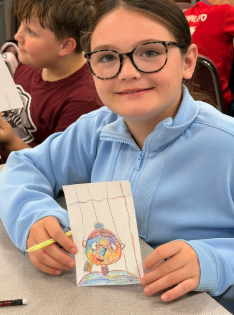 A student smiling at the camera as she displays artwork from class.