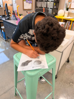 A student leans over a stool in the process of creating art in Ms. Moore's class