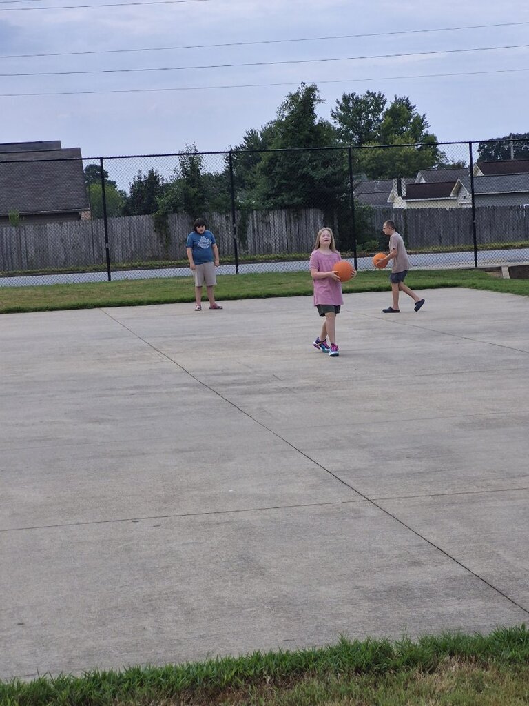 Three students are playing with basketballs outside, two students are holding the basketballs