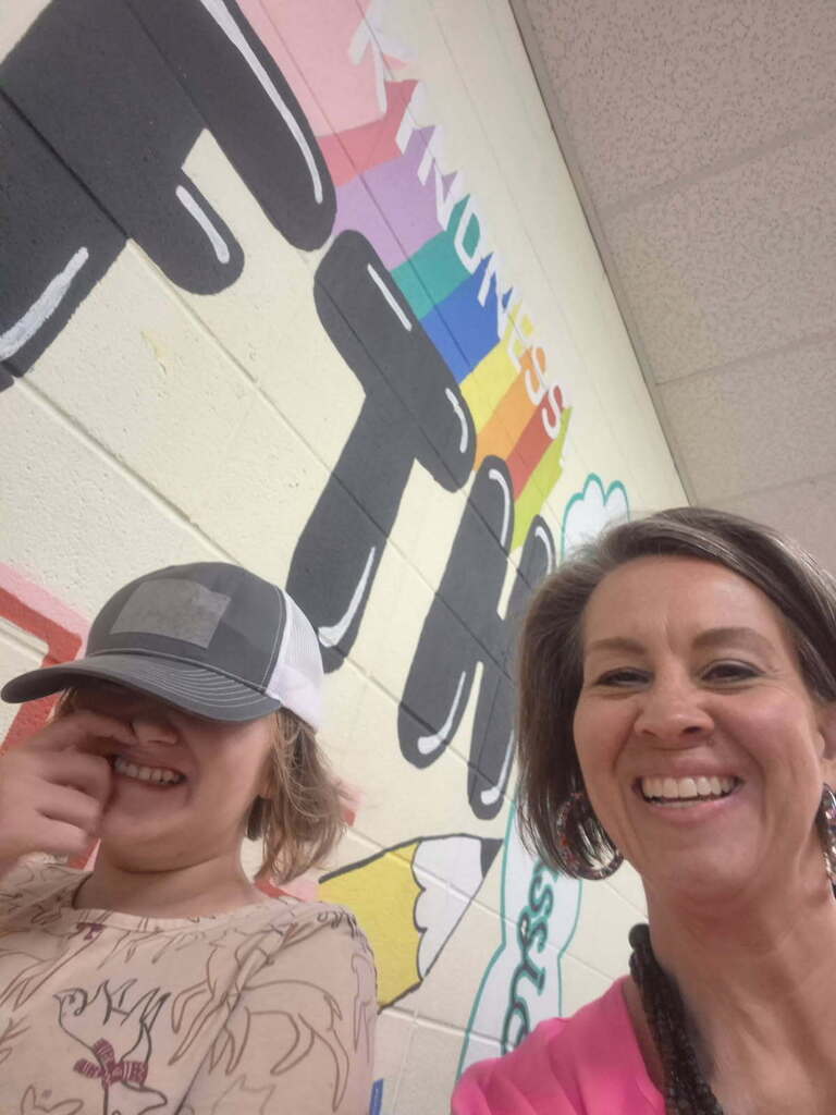 Mrs. McKell poses with a student who is smiling in the hallway