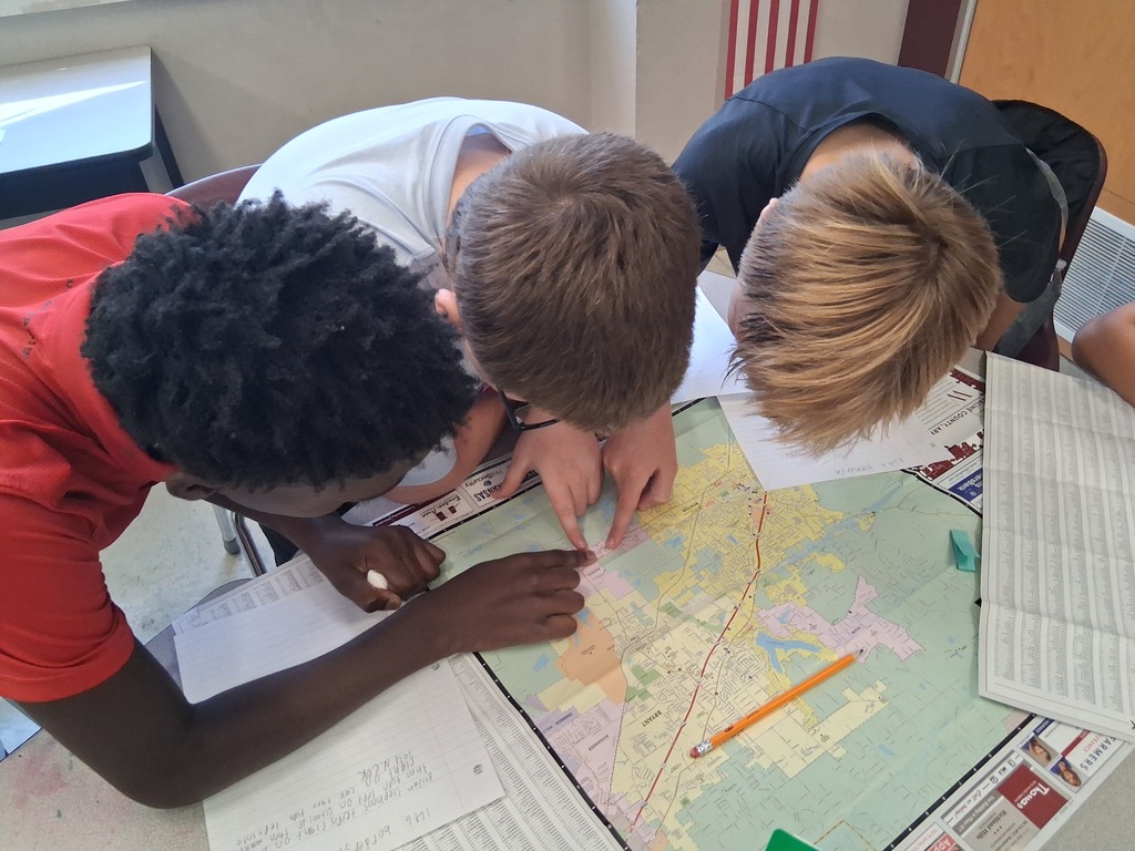 Three students stand over a map of Benton as they attempt to locate local landmarks