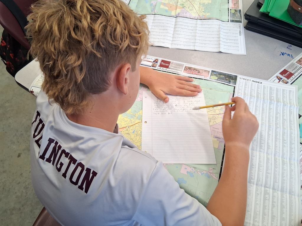 One student is seen from behind writing down answers to the map activity in social studies