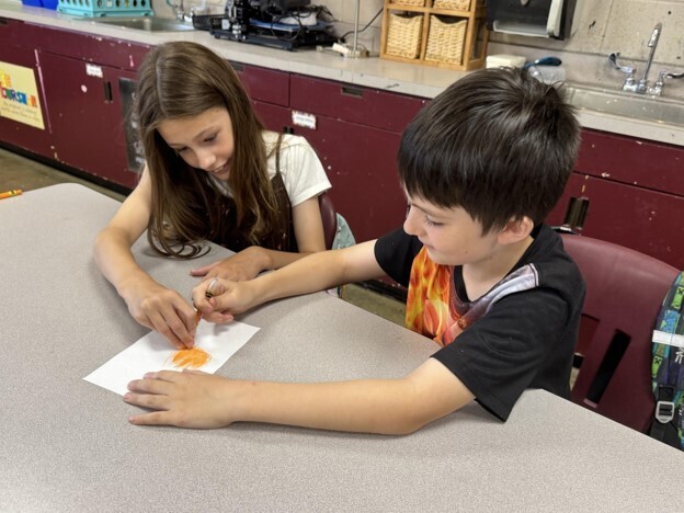 Two students participate in Mrs. Heard's 2 and a crayon activity in GT. They are both holding the same crayon as they draw a picture.