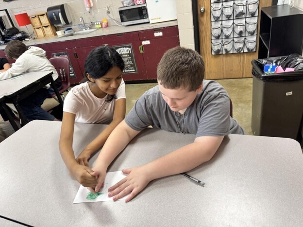 Two students participate in Mrs. Heard's 2 and a crayon activity in GT. They are both holding the same crayon as they draw a picture.