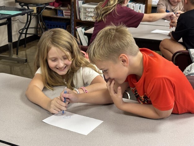 Two students participate in Mrs. Heard's 2 and a crayon activity in GT. They are both holding the same crayon as they draw a picture.