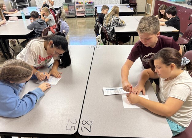 Four students participate in Mrs. Heard's 2 and a crayon activity in GT. In both teams, the students are both holding the same crayon as they draw a picture.
