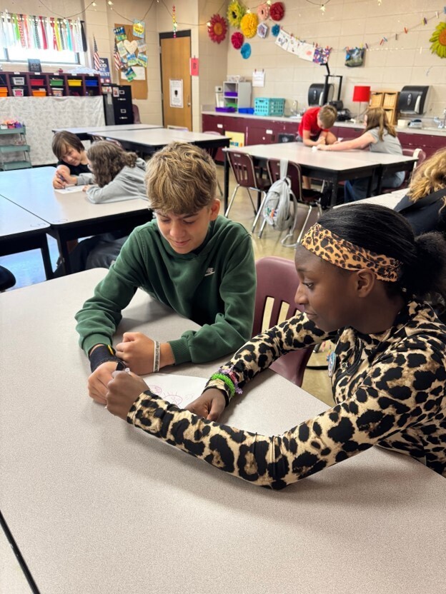 Two students participate in Mrs. Heard's 2 and a crayon activity in GT. They are both holding the same crayon as they draw a picture.