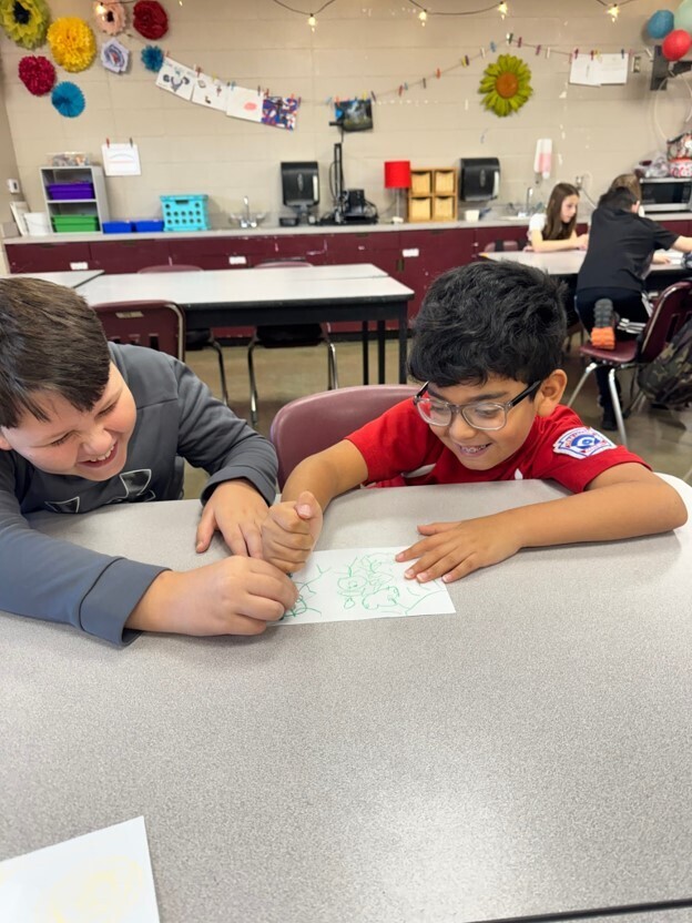 Two students participate in Mrs. Heard's 2 and a crayon activity in GT. They are both holding the same crayon as they draw a picture.