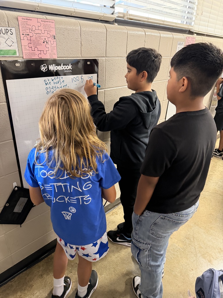 Three students work together to solve problems at chart paper on the wall of Mrs. Harris's Classroom.