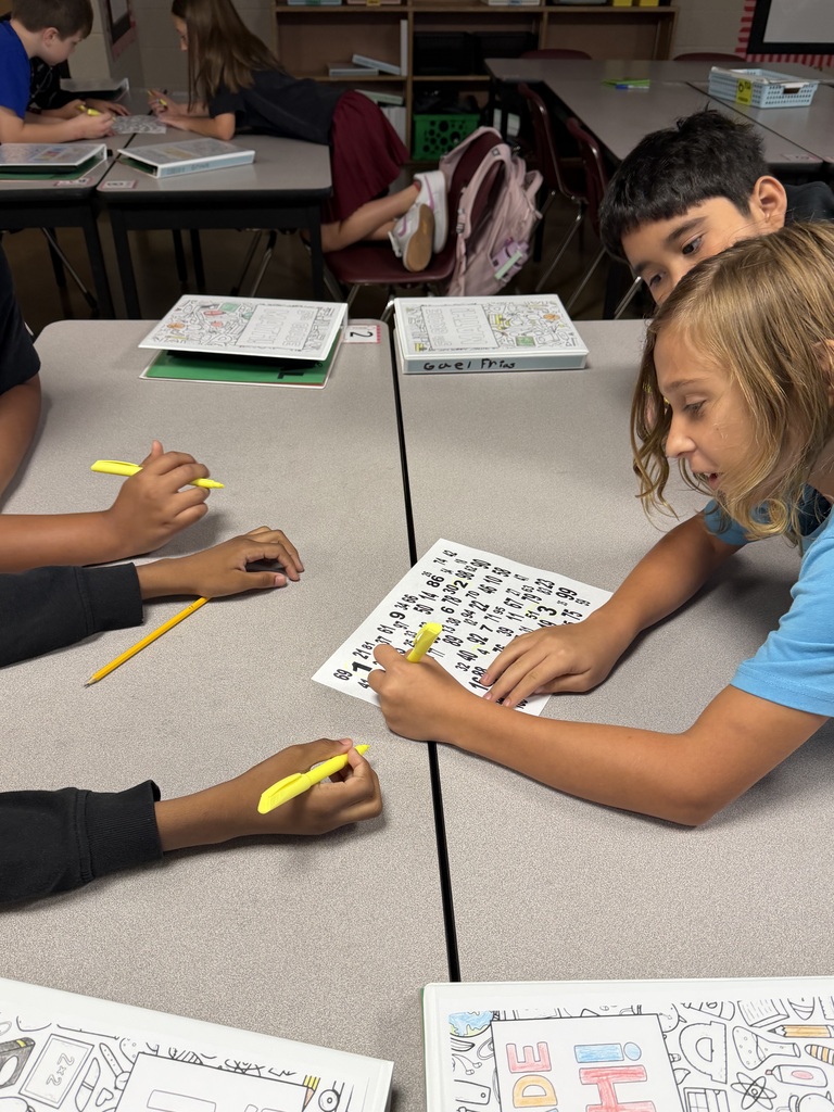 Two students huddle around a paper filled with different numbers as they work together to find numbers 1-100