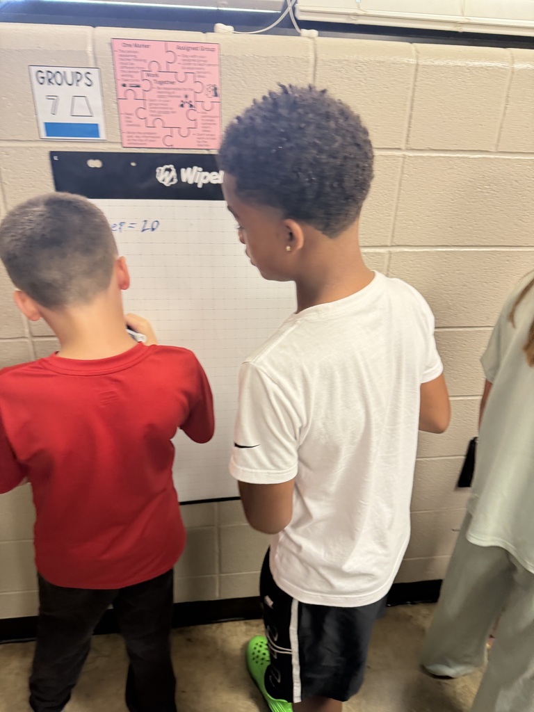 Two students work together to solve problems at chart paper on the wall of Mrs. Harris's Classroom.