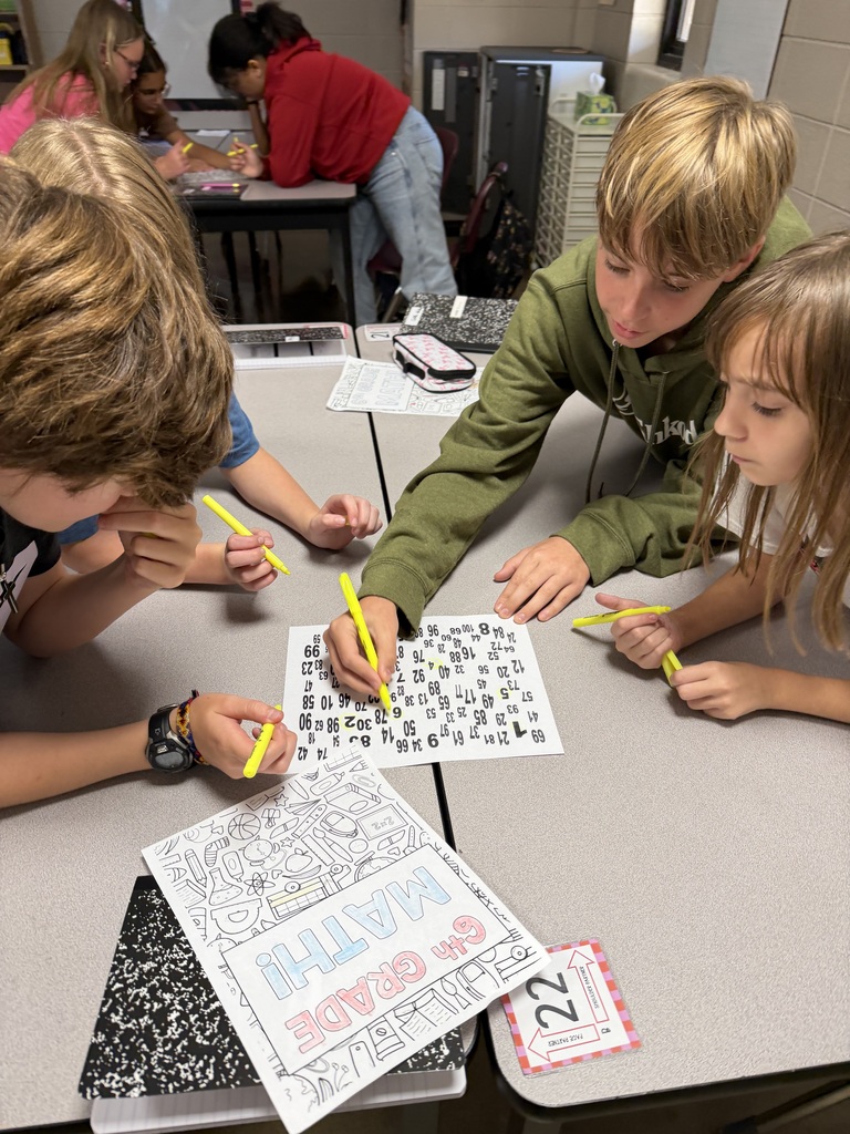 Three students huddle around a paper filled with different numbers as they work together to find numbers 1-100