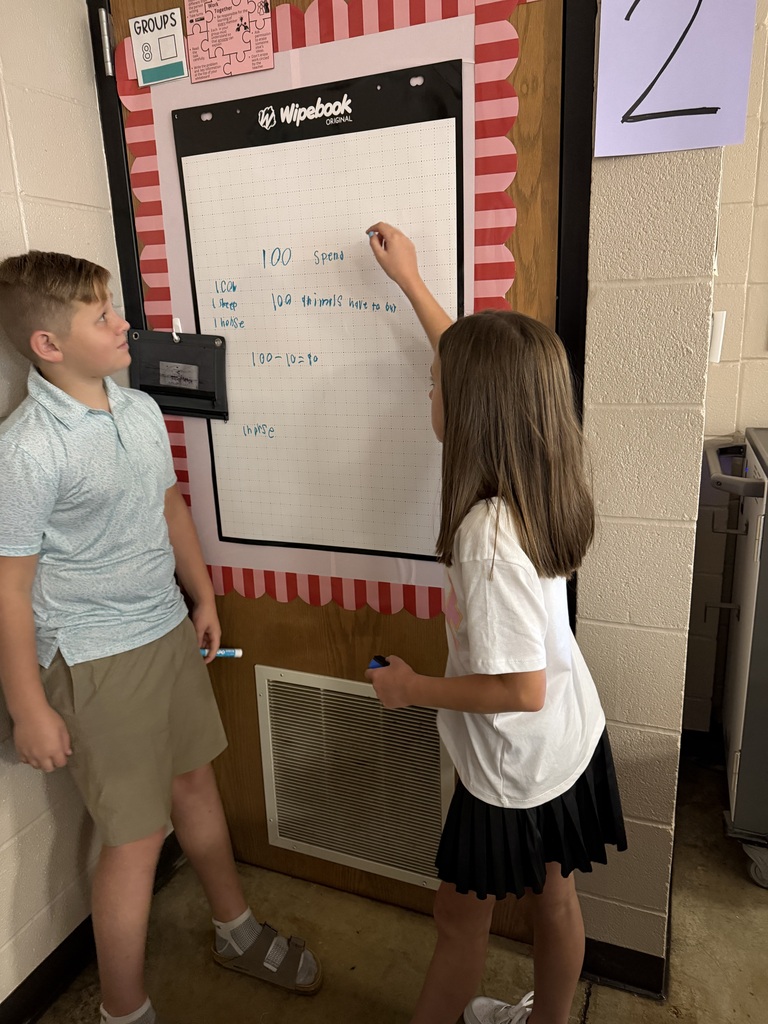 Two students work together to solve problems at chart paper on the wall of Mrs. Harris's Classroom.