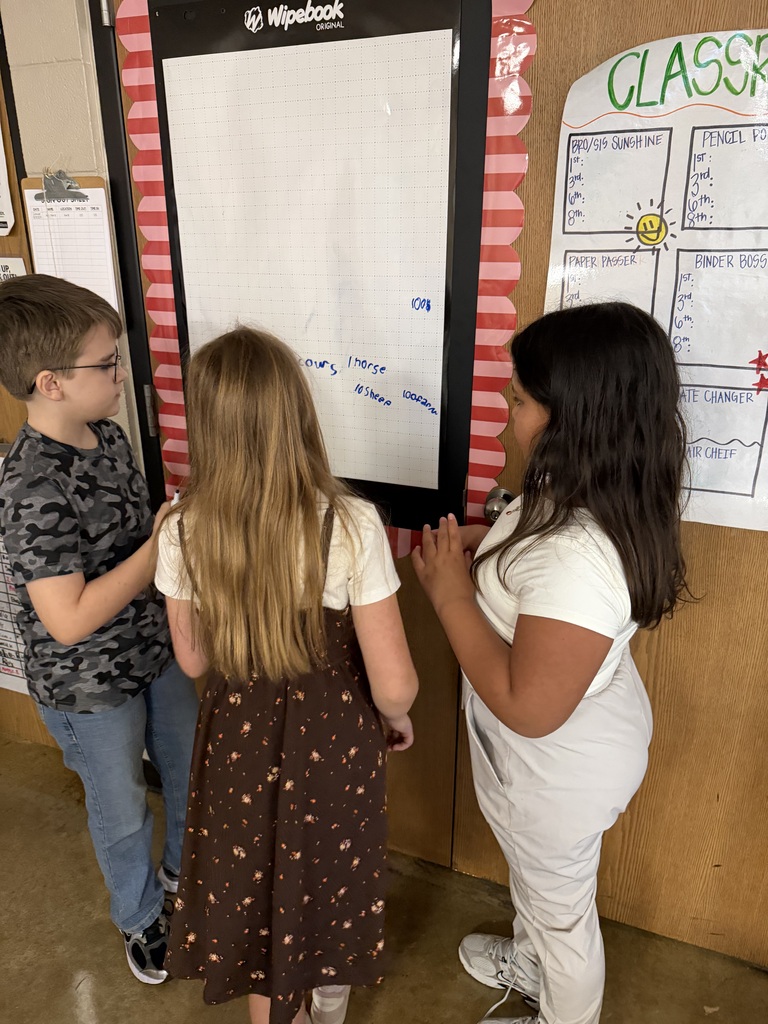 Three students work together to solve problems at chart paper on the wall of Mrs. Harris's Classroom.