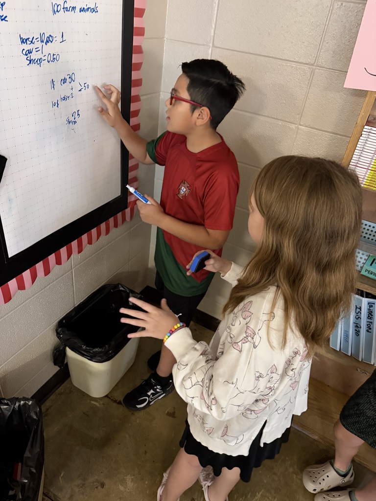 Two students work together to solve problems at chart paper on the wall of Mrs. Harris's Classroom.