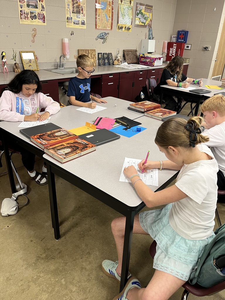 Four students gather around tables in the classroom as they work together to play a game in social studies.